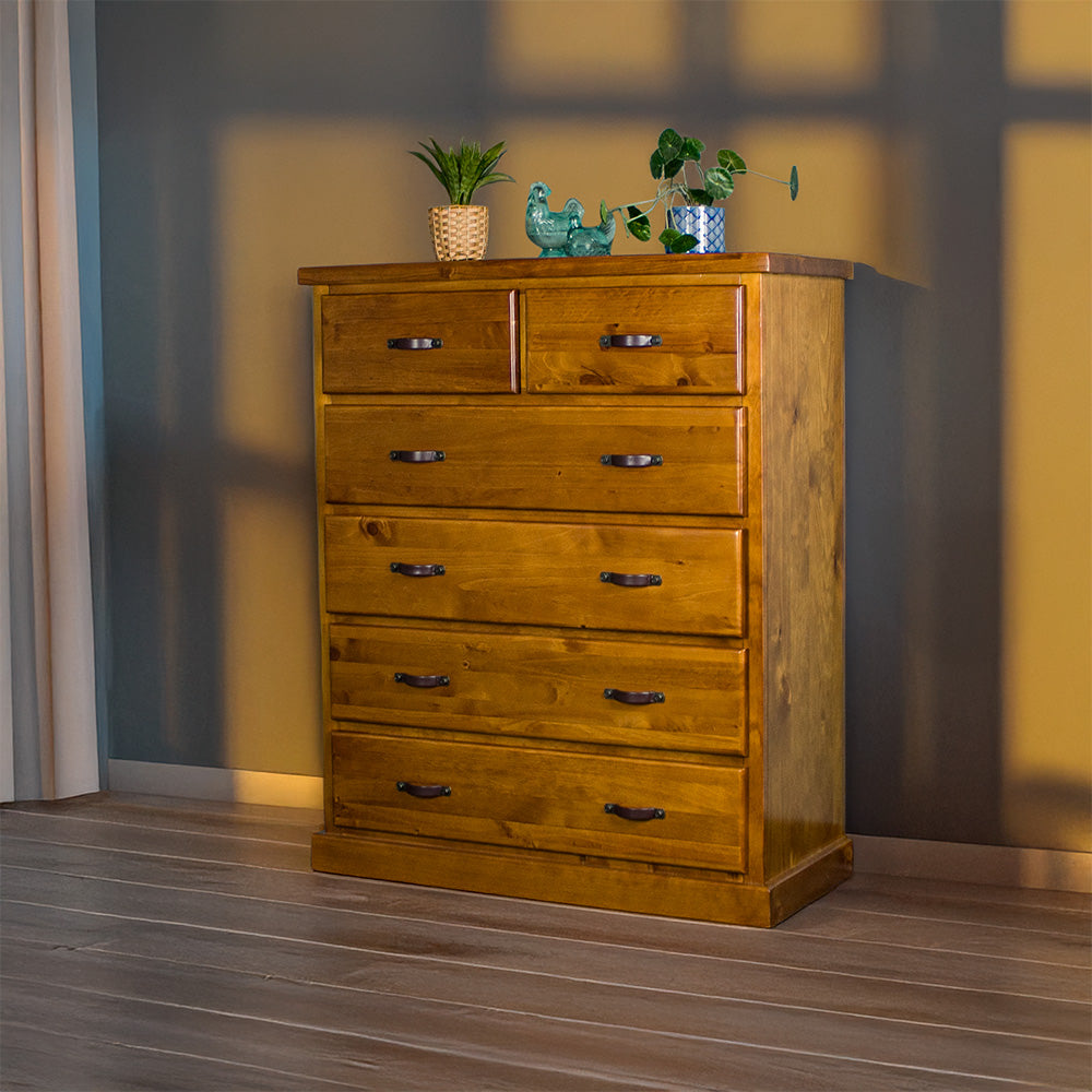 Front view of the Jamaica 6 Drawer Pine Tallboy. There are two potted plants on top and two blue glass ornaments.