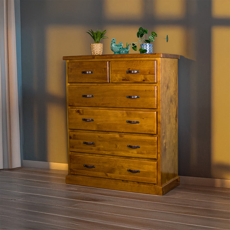 Front view of the Jamaica 6 Drawer Pine Tallboy. There are two potted plants on top and two blue glass ornaments.