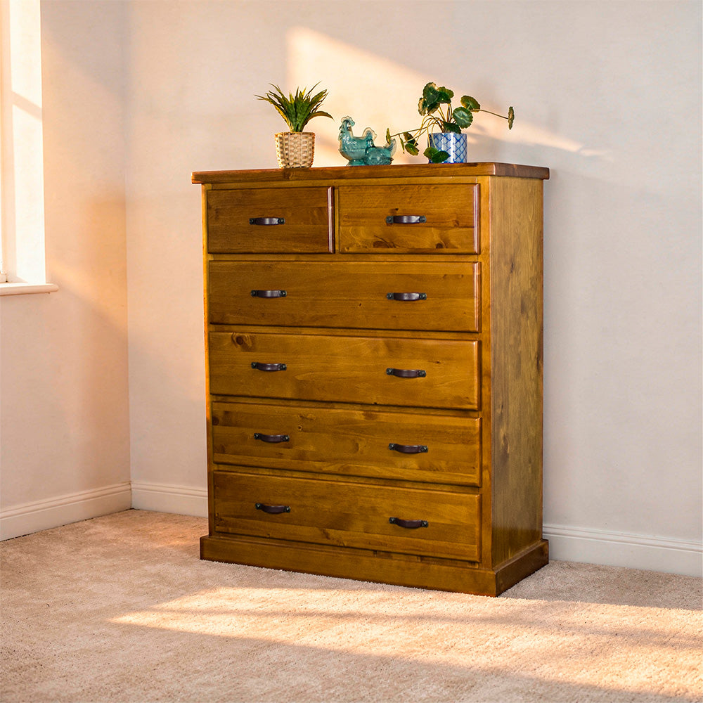 Front view of the Jamaica 6 Drawer Pine Tallboy. There are two potted plants on top and two blue glass ornaments.