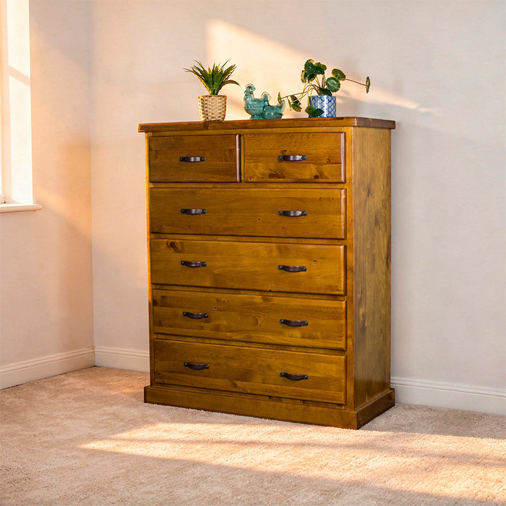 Front view of the Jamaica 6 Drawer Pine Tallboy. There are two potted plants on top and two blue glass ornaments.