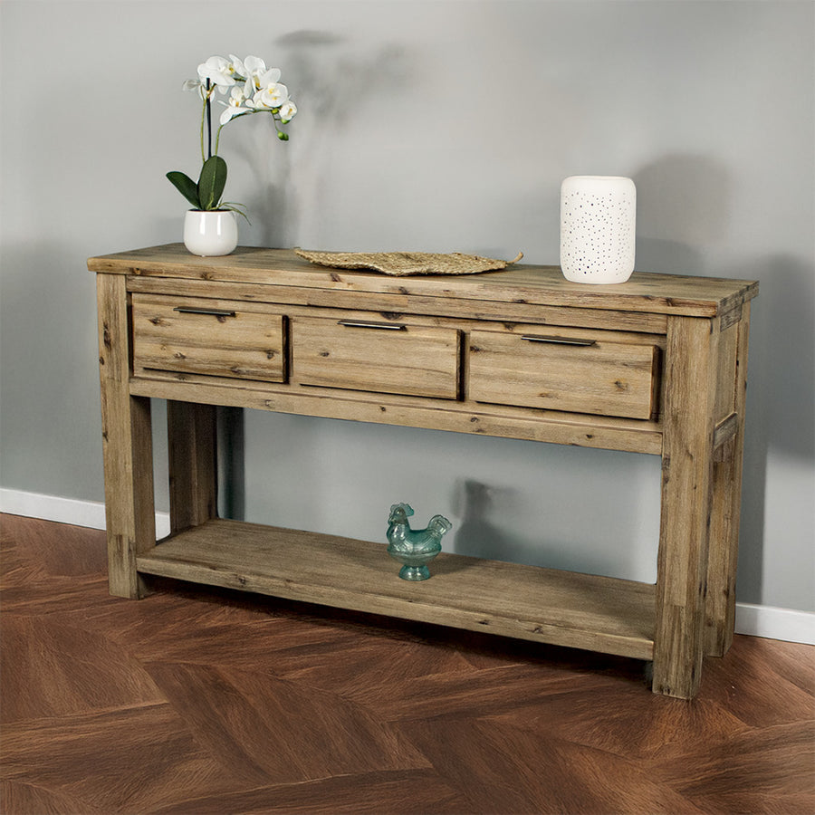 The front of the Mars 3 Drawer Console Table. There is a potted plant, a rattan leaf, and a white pot on top with a blue glass ornament on the shelf below.