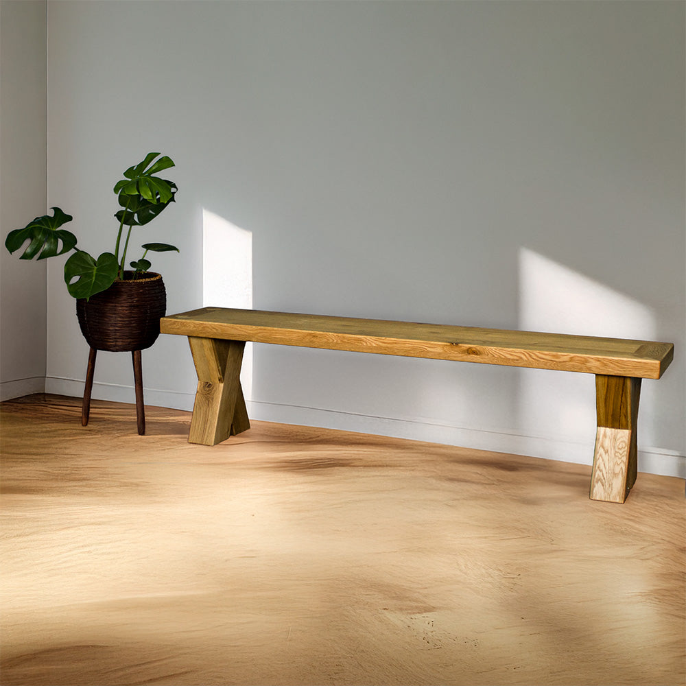 The front of the Maximus Oak Cross Leg Bench Seat (1.9m). There is a free standing potted plant next to it.