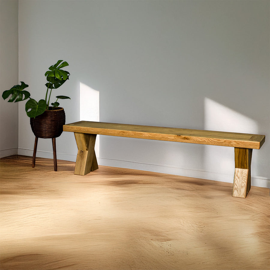 The front of the Maximus Oak Cross Leg Bench Seat (1.9m). There is a free standing potted plant next to it.