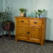 The front of the Rimu stained Montreal 2 Drawer Pine Buffet. There are two potted plants on top, with two blue glass ornaments on top.