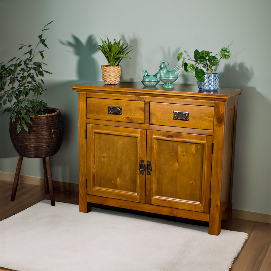 The front of the Rimu stained Montreal 2 Drawer Pine Buffet. There are two potted plants on top, with two blue glass ornaments on top.