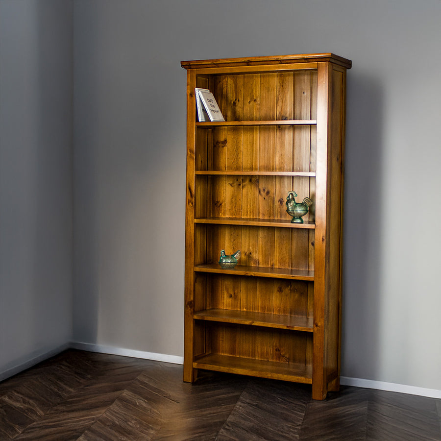 The front of the Montreal Large Pine Bookcase. There are two DVDs on the top shelf, and two blue glass ornaments on the middle two shelves. 