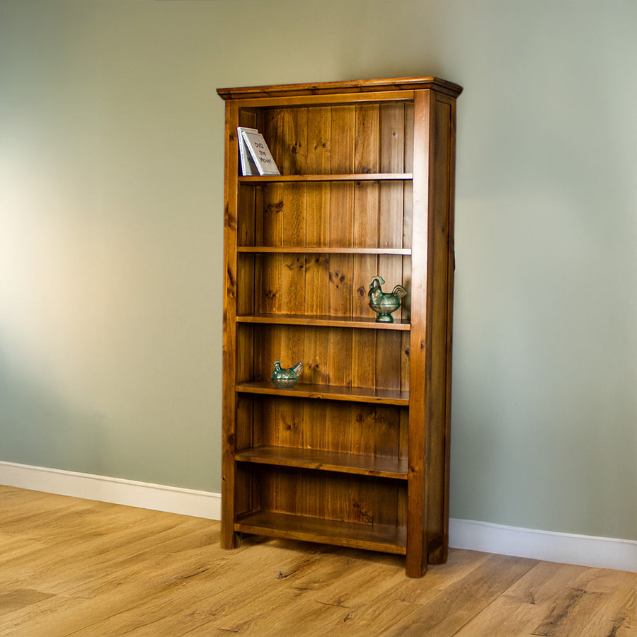 The front of the Montreal Large Pine Bookcase. There are two DVDs on the top shelf, and two blue glass ornaments on the middle two shelves. 