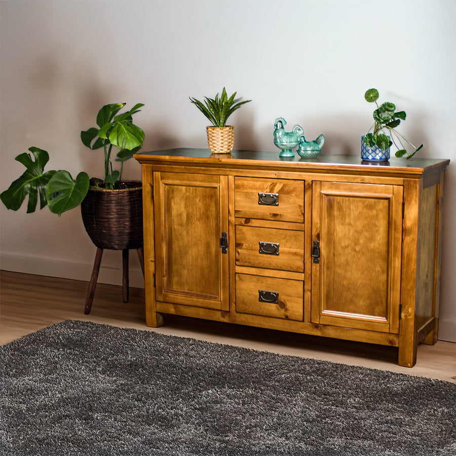 The front of the Montreal Midsize NZ Pine Buffet. There are two potted plants on top with two blue glass ornaments in between. There is a free standing potted plant next to it.