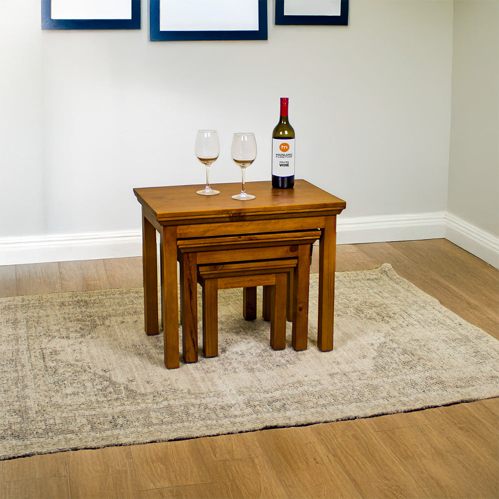 The Montreal 3 Piece Pine Nesting Tables on top of a cream coloured rug. There are two wine glasses and a bottle of wine on top.