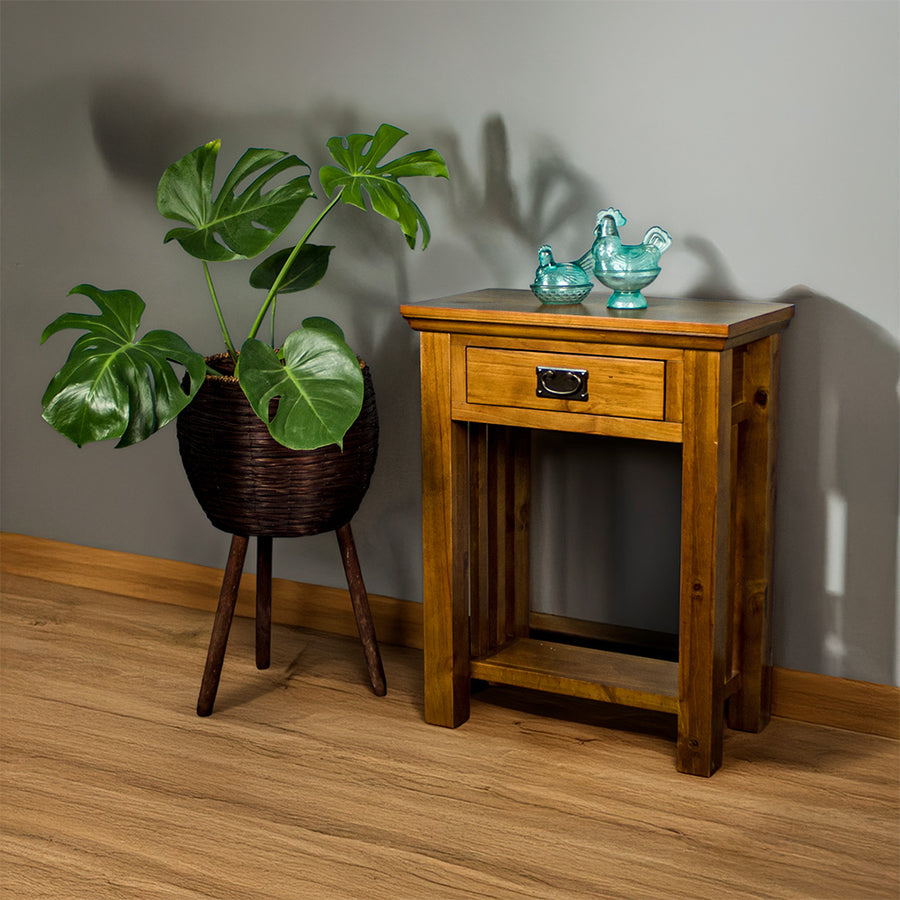 The front of the Montreal Small Pine Hall Table, with two blue glass ornaments on top. There is a free standing potted plant next to it.