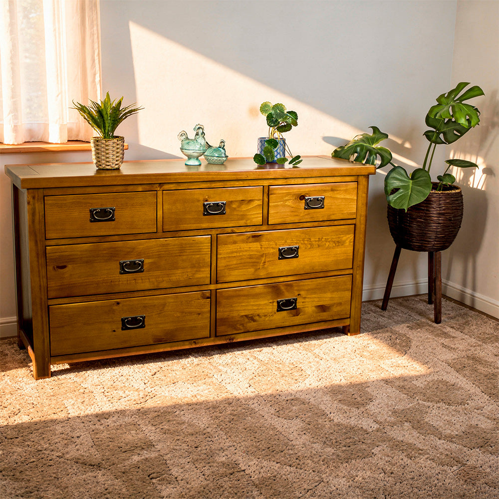 The front of the New Quebec 7 Drawer Lowboy. There are two potted plants on top with two blue glass ornaments in between. There is a free standing potted plant next to the lowboy.