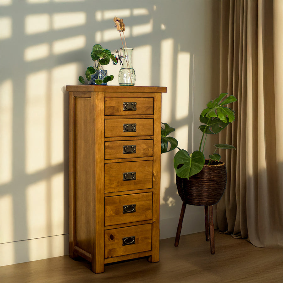 The front of the New Quebec 6 Drawer Lingerie Chest. There is a potted plant on top and a blue glass vase. There is a free standing potted plant next to it.