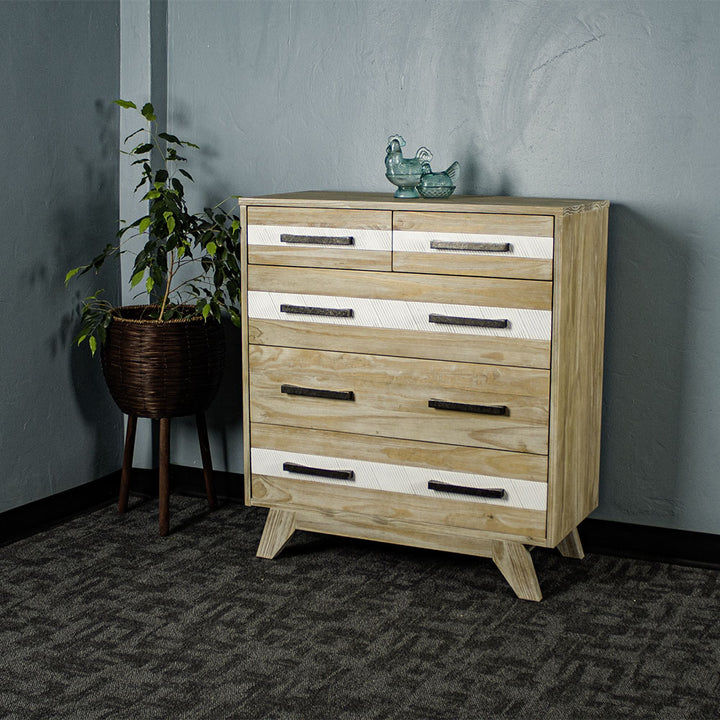 The front of the Soho 5 Drawer Tallboy. There are two blue glass ornaments on top with a free standing potted plant next to it.