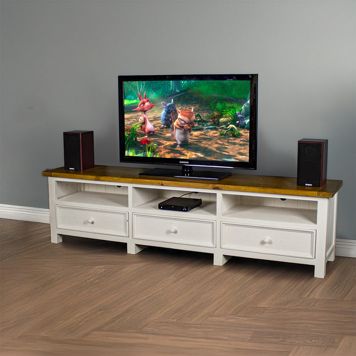 The front of the Tuscan Recycled Pine TV Unit. There is a DVD player in the middle shelf. There is a TV on top with two speakers on either side, and a free standing potted plant next to the TV stand.