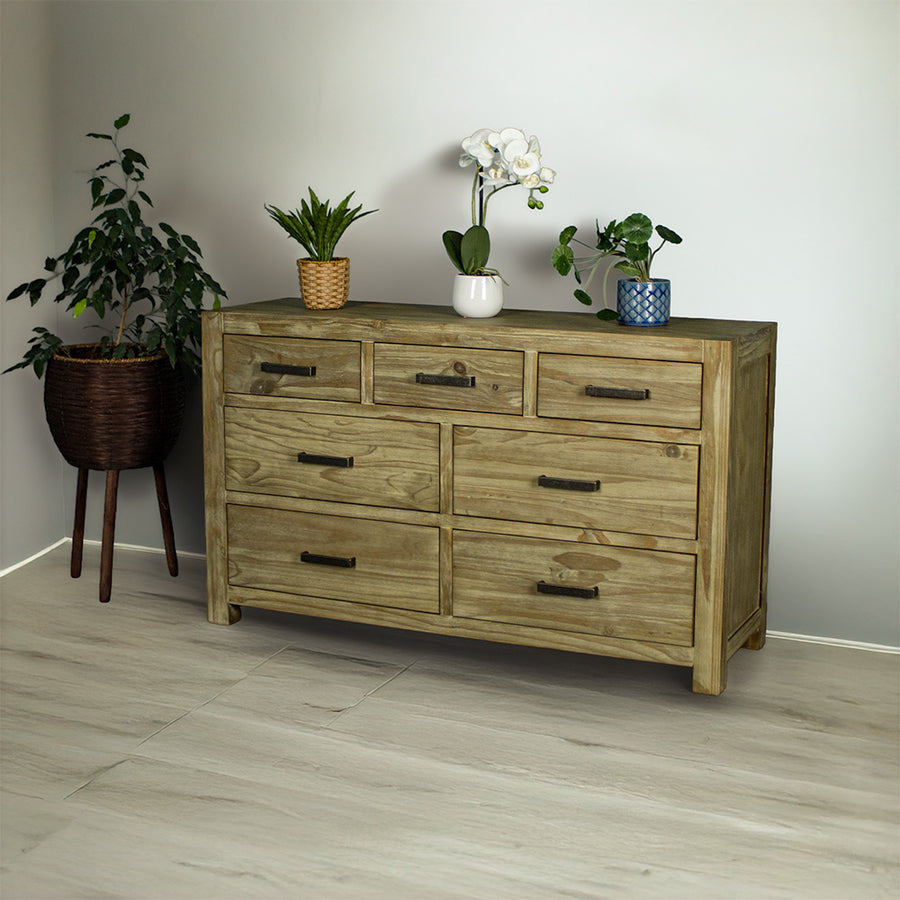 The front of the Vancouver 7 Drawer NZ Pine Lowboy. There are three potted plants on top, with a free standing potted plant next to the lowboy.