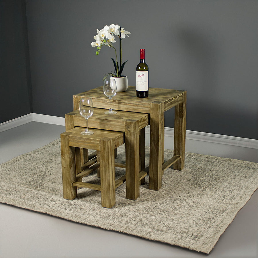The front of the Vancouver Pine Nesting Tables. There are two wine glasses, a bottle of wine and a pot of white flowers on top of the tables.