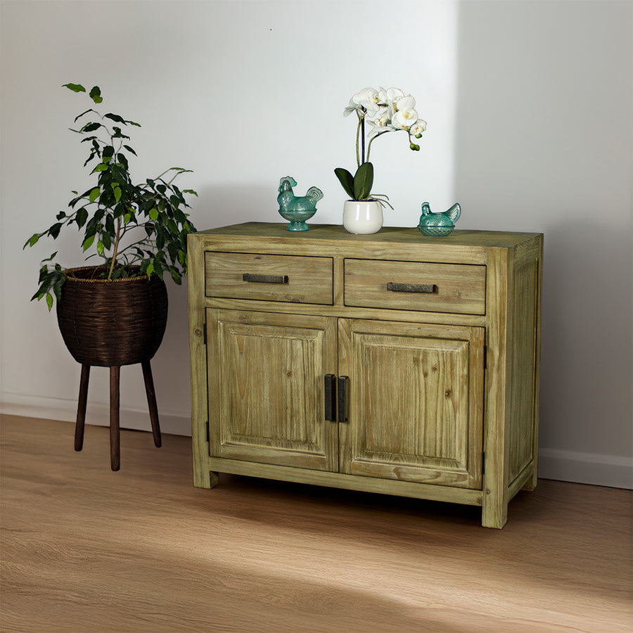 The front of the Vancouver Pine Buffet. There are two blue glass ornaments on top with a pot of white flowers in between. There is a free standing potted plant next to the buffet.