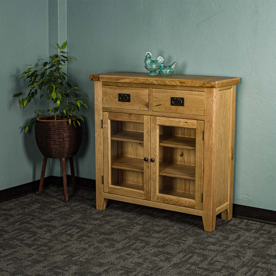 The front of the Vancouver Value 2 Drawer 2 Door Oak Sideboard. There are two blue glass ornaments on top  and a free standing potted plant next to the buffet.