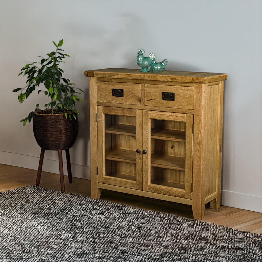 The front of the Vancouver Value 2 Drawer 2 Door Oak Sideboard. There are two blue glass ornaments on top  and a free standing potted plant next to the buffet.