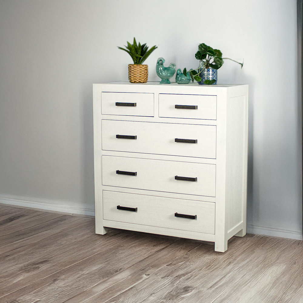 Vancouver Five Drawer White NZ Pine Tallboy front view. There are two potted plants on top and two blue glass ornaments.