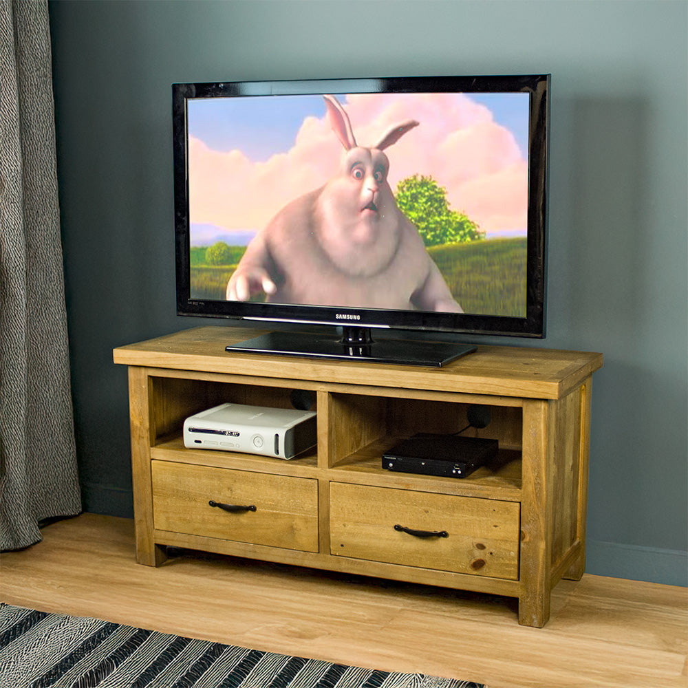 The front of the Ventura Two Drawer Recycled Pine TV Unit. There is a large TV on top, and two media devices in each shelf above the drawers.
