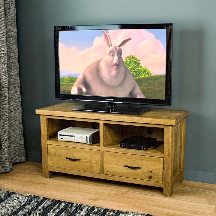 The front of the Ventura Two Drawer Recycled Pine TV Unit. There is a large TV on top, and two media devices in each shelf above the drawers.