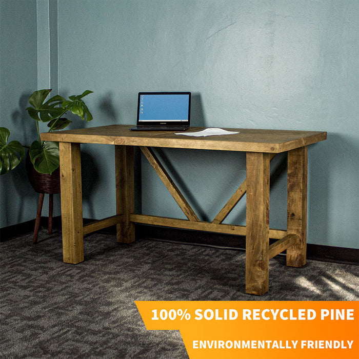 Front view of the Ventura Recycled Pine Desk. There is a laptop and a pile of papers on top. There is a free standing potted plant next to the desk.