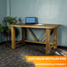 Front view of the Ventura Recycled Pine Desk. There is a laptop and a pile of papers on top. There is a free standing potted plant next to the desk.