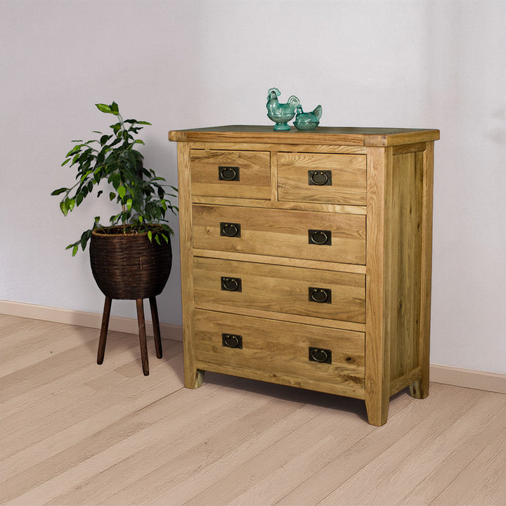 The front of the Yes Five Drawer Oak Chest with two blue glass ornaments on top. There is a free standing potted plant next to the tallboy.