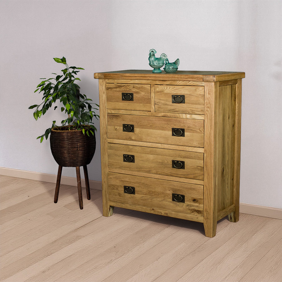 The front of the Yes Five Drawer Oak Chest with two blue glass ornaments on top. There is a free standing potted plant next to the tallboy.