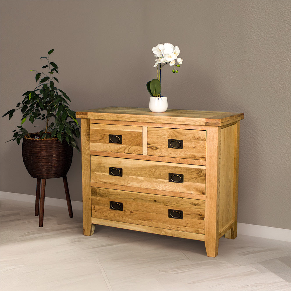 The front of the Yes Four Drawer Oak Lowboy, there is a small pot of white flowers on top and a free standing potted plant next to the lowboy.