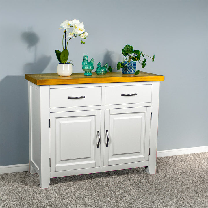 The front of the Felixstowe Small Pine Buffet (White). There are two potted plants with two blue glass ornaments in between on top of the sideboard.