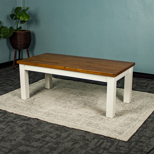 The Alton Mid Size Coffee Table on a rug. There is a free standing potted plant in the back.