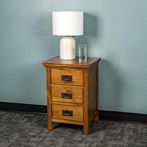 The front of the Montreal Pine Bedside Cabinet. There is a lamp and a glass of water on top.