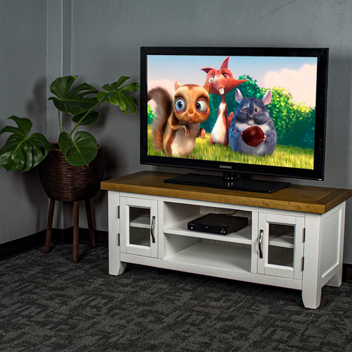 The front of the Felixstowe 2 Door Entertainment Unit (White). There is a DVD player in the top shelf in the middle and a large TV on top. There is a free standing potted plant next to the TV Unit.