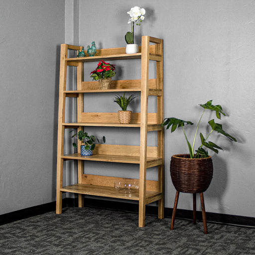 The front of the Kubic Oak Display Shelf. There are two blue glass ornaments and a pot of white flowers on the top shelf, a bundle of red flowers on the second shelf, a potted plant on the third shelf, a potted plant on the fourth shelf and a glass bowl on the fifth shelf. There is a free standing potted plant next to the shelf.