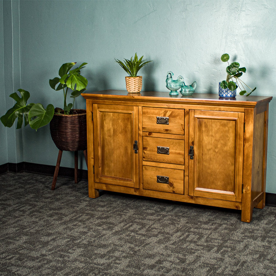 The front of the Montreal Midsize NZ Pine Buffet. There are two potted plants on top with two blue glass ornaments in between. There is a free standing potted plant next to it.