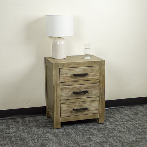 The front of the stonewash Vancouver 3 Drawer Bedside Cabinet. There is a lamp and a glass of water on top.