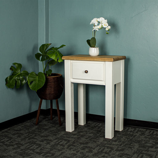The front of the Loire Oak Console Table. There is a pot of white flowers on top and a free standing potted plant to the left.