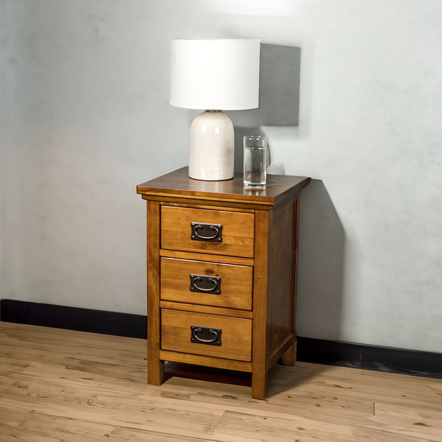 The front of the Montreal Pine Bedside Cabinet. There is a lamp and a glass of water on top.