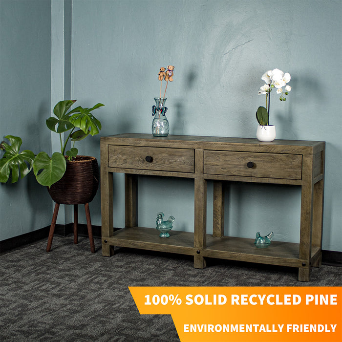 Front view of the brown Stonemill Recycled Pine Hall Table with black circular handles. There are two blue glass ornaments on the lower shelf and two potted plants on the top. There is text in the bottom right corner that says "100% Solid Recycled Pine" and "Environmentally Friendly"