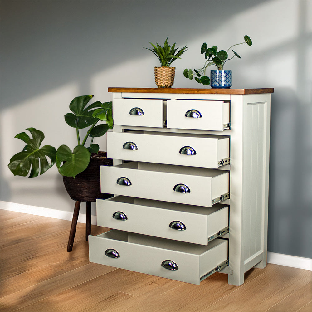 An overall view of the Alton 6 Drawer NZ Pine Tallboy with its drawers open. There is a free standing potted plant next to it. There are two potted plants on top