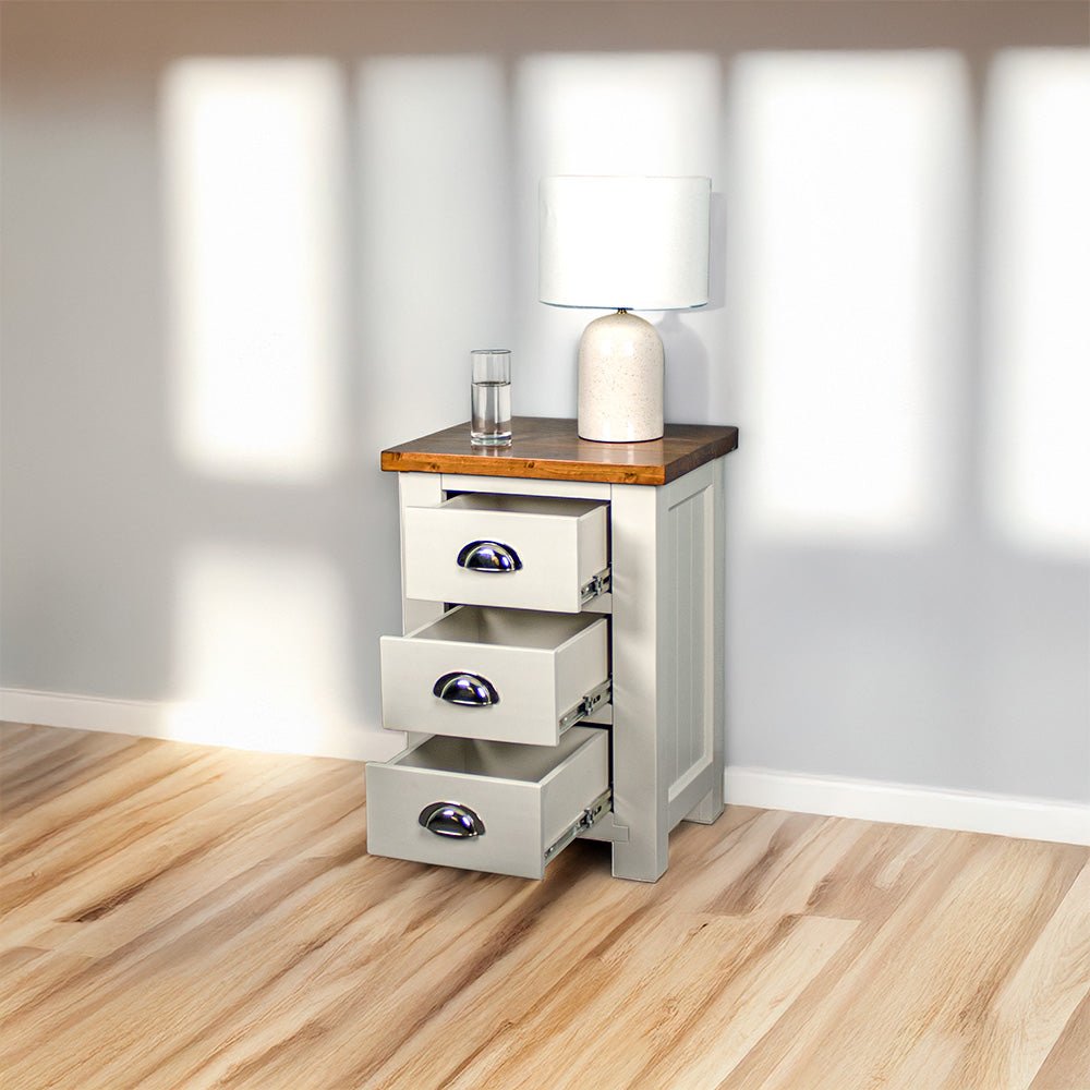 The Alton 3 Drawer Pine Bedside Cabinet with a Rimu stained top has its drawers open. There is a lamp on the top. It is next to a free standing potted plant.