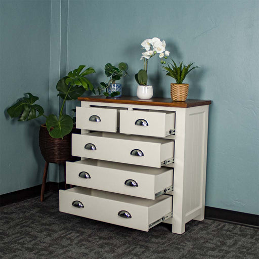 The front of the Alton 5 Drawer Pine Tallboy with its drawers open. There is a free standing potted plant next to it. There are three potted plants on top.