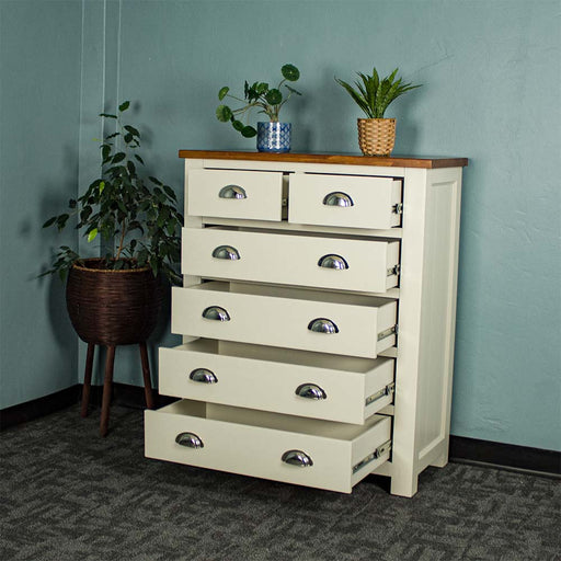 An overall view of the Alton 6 Drawer NZ Pine Tallboy with its drawers open. There is a free standing potted plant next to it. There are two potted plants on top