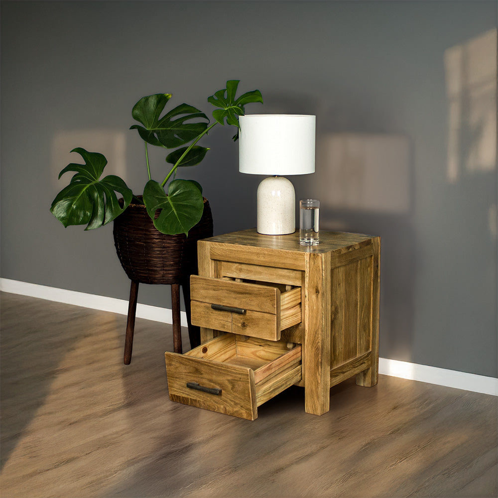 The front of the Amalfi 2-Drawer Oak Bedside with its drawers open. There is a free standing potted plant next to it. There is a lamp and a small glass of water on top.