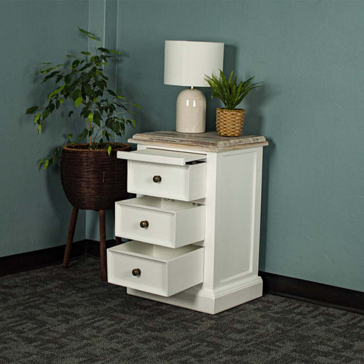 The front of the Biarritz 3 Drawer Bedside Cabinet with its drawers out. There is a lamp and a potted plant on top with a free standing potted plant next to the bedside table.