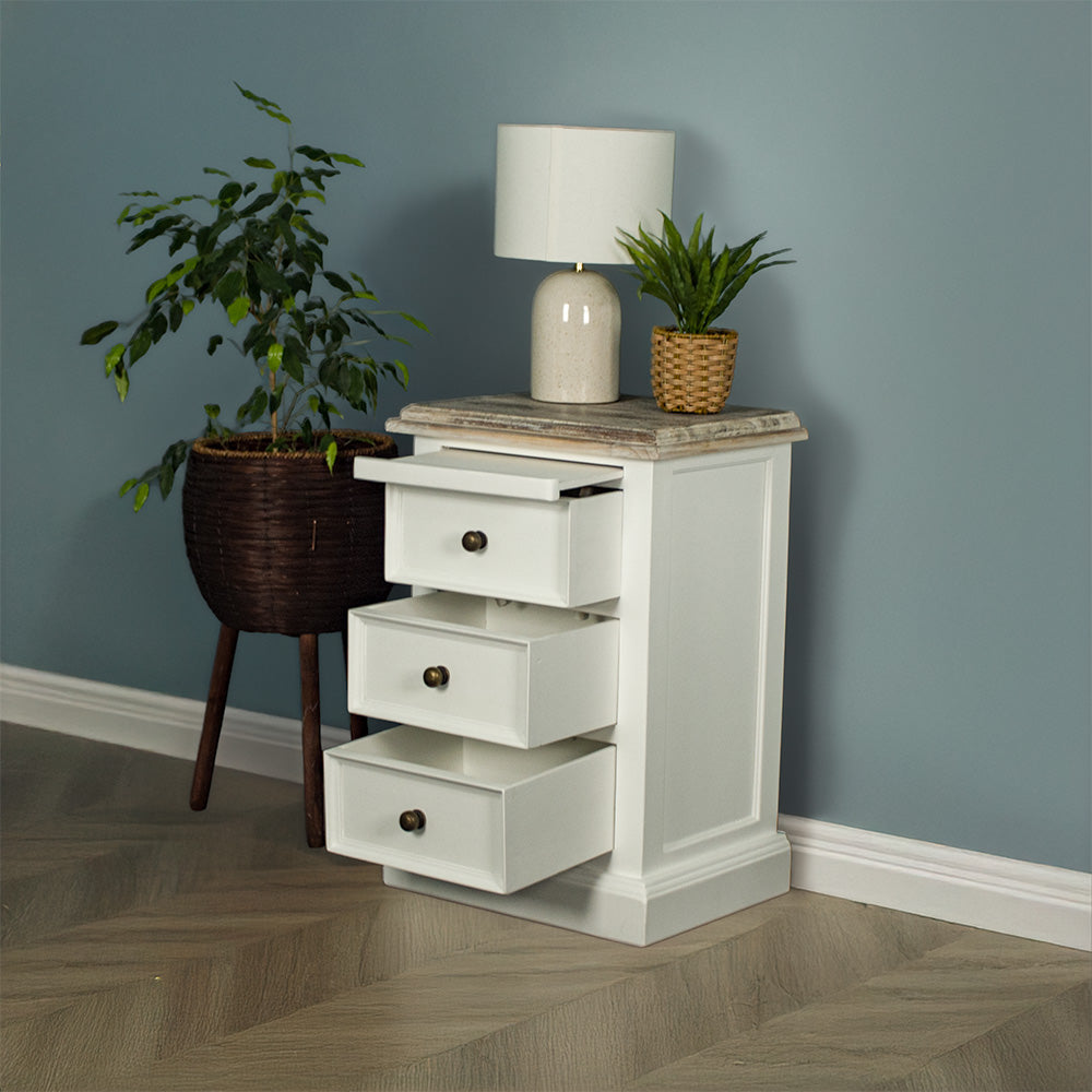 The front of the Biarritz 3 Drawer Bedside Cabinet with its drawers out. There is a lamp and a potted plant on top with a free standing potted plant next to the bedside table.