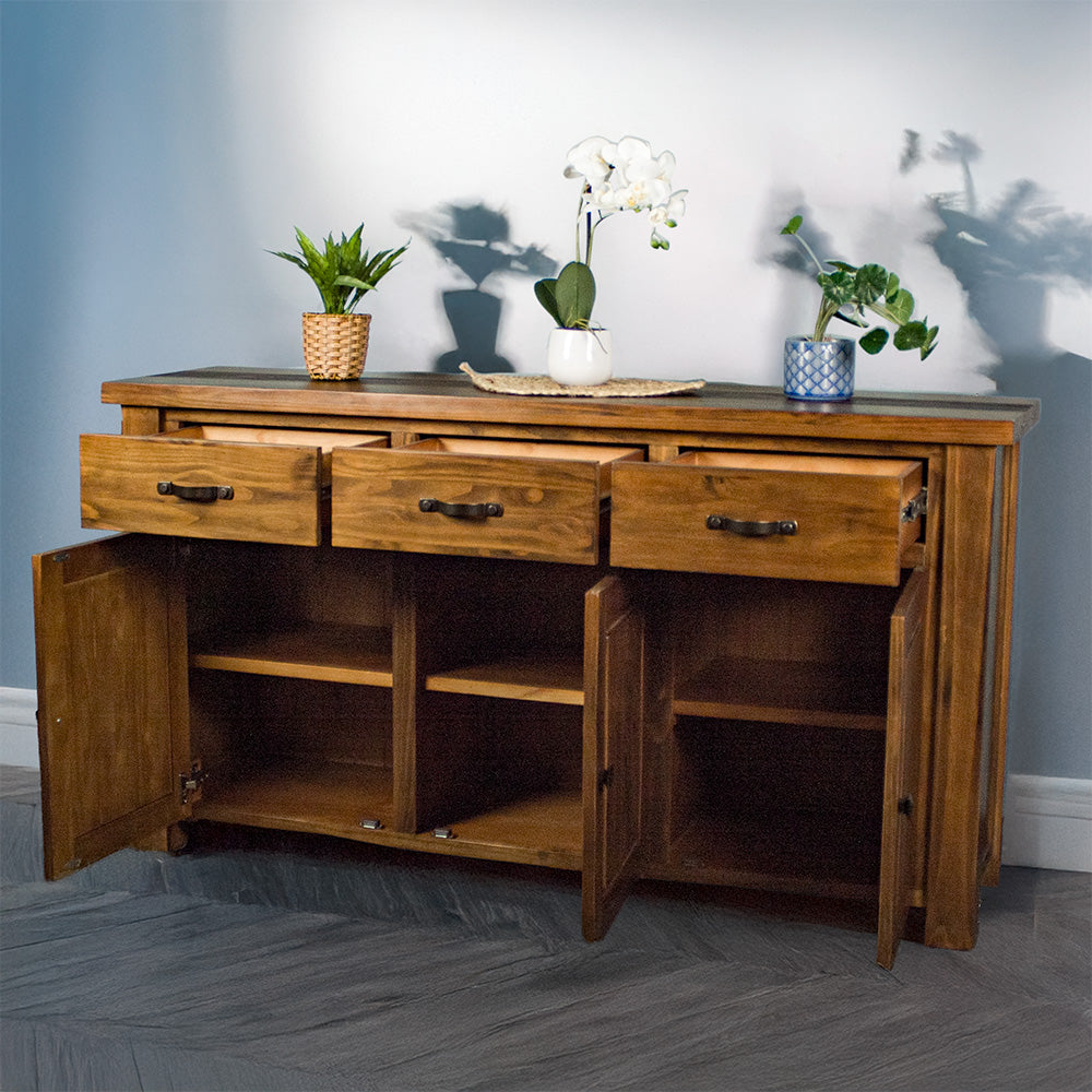 The front of the Botanica 3-Drawer Large Buffet, with its drawers and doors open. There are three potted plants on top, with the middle one on top of a rattan leaf.