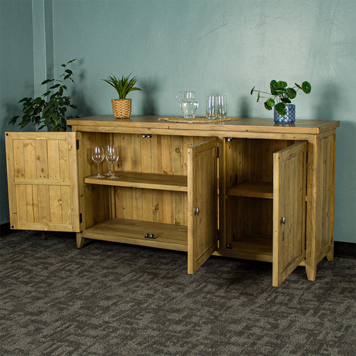 An overall view of the Cairns Recycled Pine Buffet with its doors open. There is a tall free standing potted plant next to the unit. There are two small potted plants on top on either side, inbetween a small pitcher of water and two glasses.